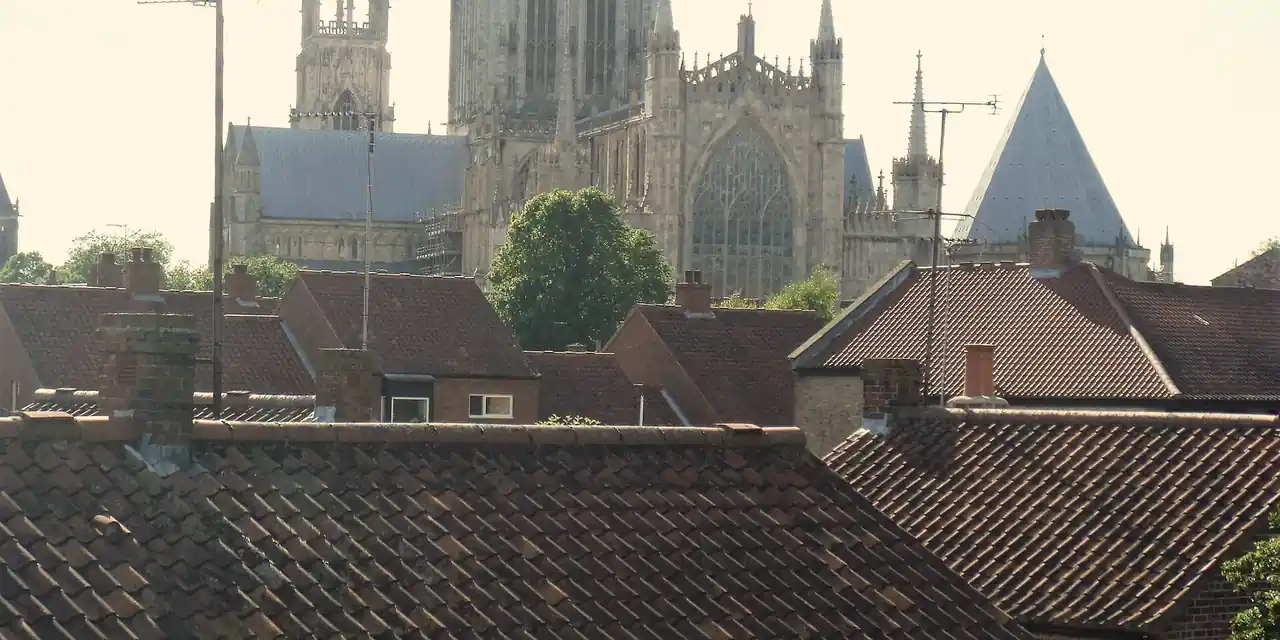 Weathered red clay pantile roofs and brick chimneys in York with York Minster rising behind