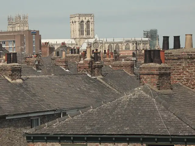 Weathered slate roofs, chimney stacks and clay pots across York terraces with York Minster in the distance